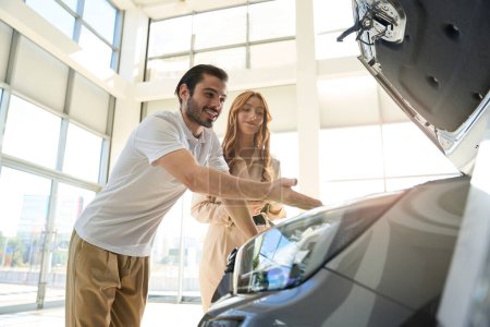 Téléchargez les photos : Acheteur automobile pointant vers les pièces de voiture sous capot à vendeuse dans la salle d'exposition - en image libre de droit