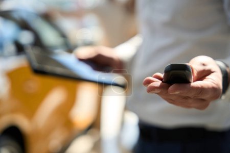 Téléchargez les photos : Photo floue du vendeur de voiture tenant le porte-clés automatique et l'ordinateur tablette dans les mains - en image libre de droit