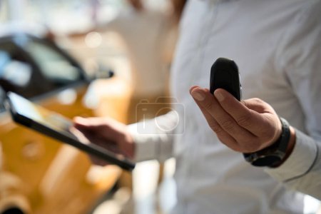 Photo for Cropped photo of salesclerk holding car key fob and tablet computer in hands - Royalty Free Image