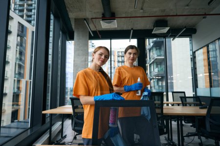 Photo for Young women are in the office area in work clothes and rubber gloves, they have wipes and cleaning products - Royalty Free Image