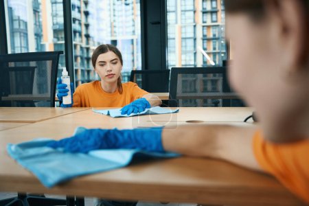 Photo for Women in uniform and rubber protective gloves wash wooden tables in the office with a special napkin - Royalty Free Image