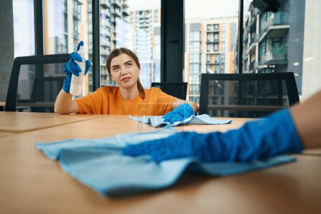 Photo for Cute cleaning company employees in uniform and rubber protective gloves disinfect desktops in the office with a special napkin - Royalty Free Image