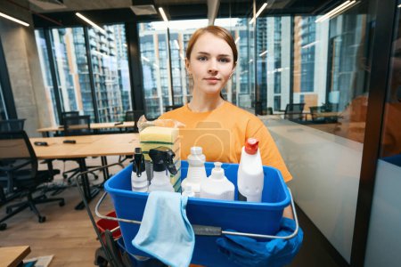 Young woman holds a professional cleaning and disinfection kit in her hands - a bucket, sponges, spray, napkins, detergents