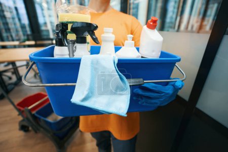 Téléchargez les photos : Service de nettoyage des employés tient seau dans ses mains avec un ensemble de gadgets de nettoyage et de désinfection éponges, spray, serviettes, détergents - en image libre de droit