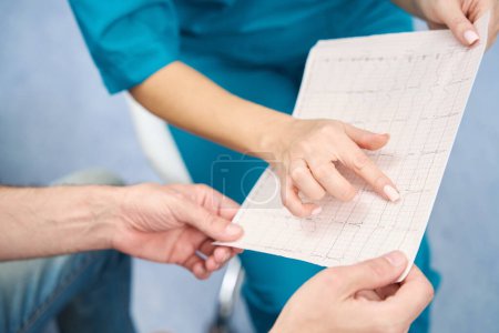 Photo for Nurse and patient sitting next to friend and discussing electrocardiogram results - Royalty Free Image