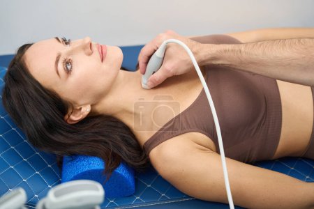 Angespannte Patientin unterzieht sich einem Schilddrüsentest, während der Arzt den Sensor der Maschine auf ihren Hals richtet