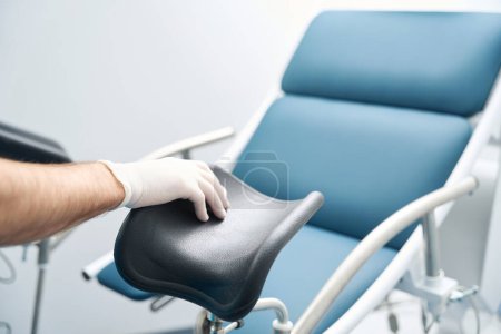 Foto de La mano de un trabajador médico en un guante estéril toca la silla para examinar al paciente - Imagen libre de derechos