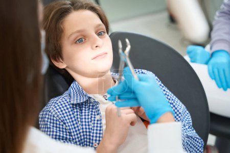 Foto de Asustado joven paciente en una silla en el dentista, el médico preparó una herramienta para la extracción de dientes - Imagen libre de derechos