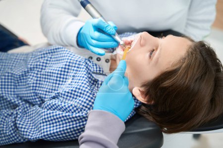 Photo for Boy is being treated for tooth at a dentist in medical institution, the doctor uses an endomotor in his work - Royalty Free Image
