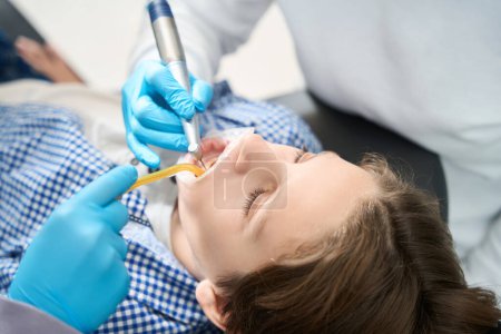 Téléchargez les photos : Adolescent à un rendez-vous chez le dentiste dans un établissement médical, le médecin utilise un endomoteur dans son travail - en image libre de droit