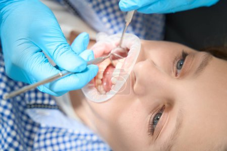 Téléchargez les photos : Dentiste effectue un nettoyage professionnel des dents de garçon dans des gants de protection, le médecin utilise des outils spéciaux - en image libre de droit