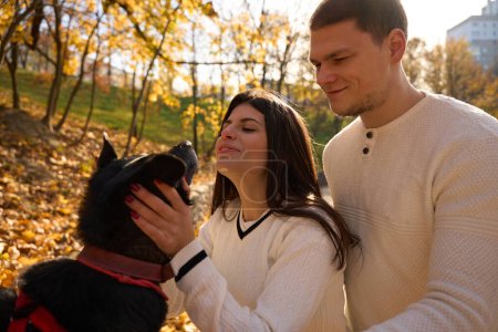 Téléchargez les photos : Jeune couple joyeux promenant leur chien dans le parc, femme embrassant l'animal de compagnie - en image libre de droit