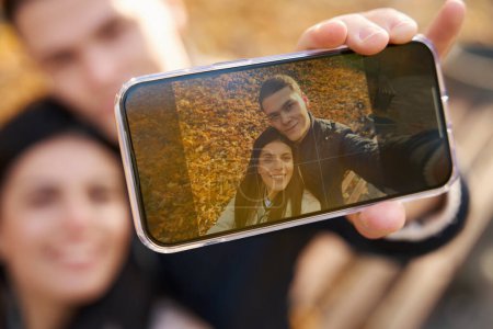 Foto de Feliz joven pareja toma una selfie en el parque de otoño, que suavemente se abrazaron el uno al otro - Imagen libre de derechos