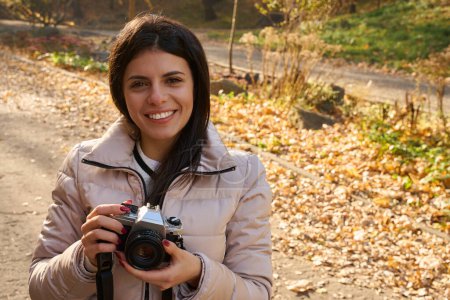 Foto de Fotografía de una joven sonriente con una cámara en las manos sobre el telón de fondo de un paisaje otoñal - Imagen libre de derechos