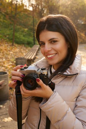 Photo for Shot of a beautiful young woman with a camera in her hands, she is in the autumn park - Royalty Free Image