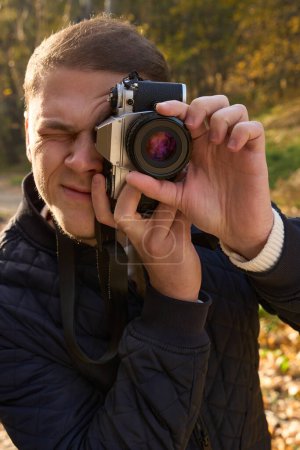 Téléchargez les photos : Jeune homme tient une caméra sur son visage, il prend une photo mémorable - en image libre de droit