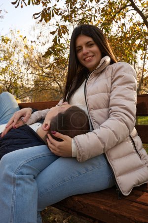 Foto de Pareja joven se encuentra en un banco del parque, el tipo puso su cabeza en las rodillas de su novia - Imagen libre de derechos