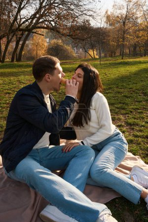 Téléchargez les photos : Joyeux jeune couple assis sur la pelouse dans le parc de la ville, les gars se font plaisir à des bonbons - en image libre de droit