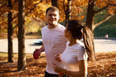 Fröhliche junge Leute unterhalten sich beim Joggen im Park, in den Händen eines Mannes liegt eine Roulette-Leine