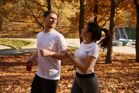 Téléchargez les photos : Beau mec et sa jeune copine font du jogging dans le parc, dans les mains d'un homme une laisse de roulette - en image libre de droit