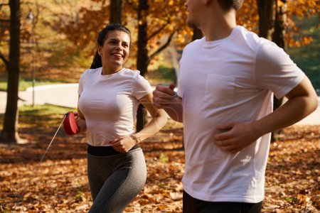Photo for Handsome guy and his happy girlfriend on morning jog in the park, in hands of woman a tape measure leash - Royalty Free Image