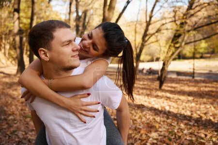 Photo for Big and strong guy rides his slender girlfriend on backs, they frolic in a beautiful park - Royalty Free Image