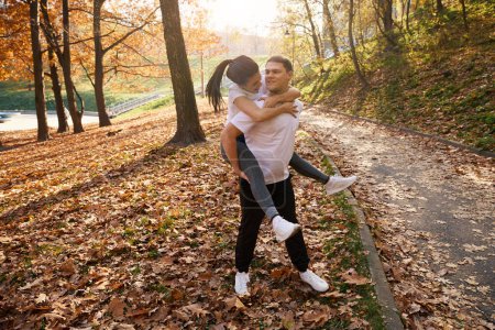 Photo for Cheerful female student in the park rides on the backs of a friend, around the golden autumn - Royalty Free Image