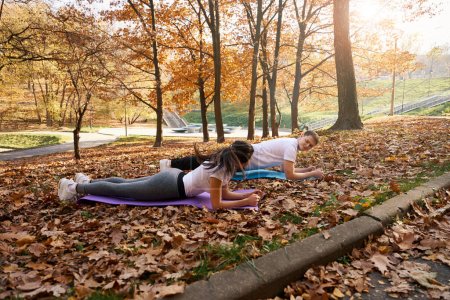 Photo for Young people do a plank on carimats in the park, golden autumn around - Royalty Free Image
