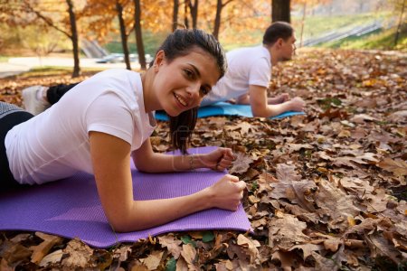 Photo for Dark-haired student and her friend are doing yoga on karimats in the park, fallen leaves around - Royalty Free Image