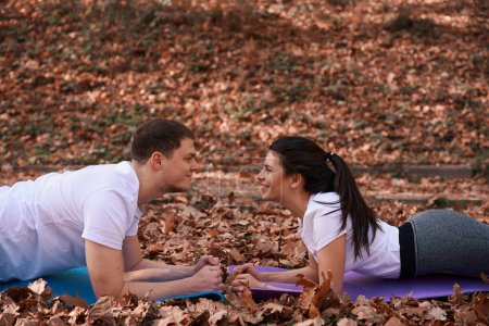 Photo for Cheerful guy and his girlfriend look at each other, they lie on karimats among autumn foliage - Royalty Free Image