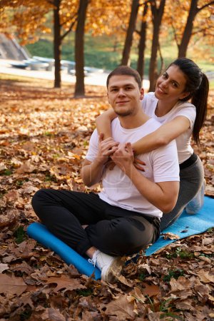 Photo for Satisfied guy and his smiling girlfriend are sitting on carimate in the park, autumn trees around - Royalty Free Image