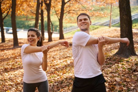 Foto de Hombre y mujer alegres haciendo ejercicios matutinos en un parque de la ciudad entre árboles otoñales - Imagen libre de derechos