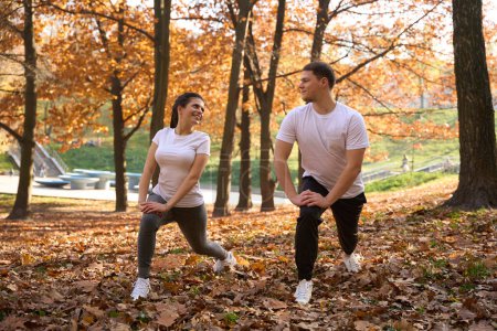 Téléchargez les photos : Couple joyeux fait un échauffement dans le parc, il ya beaucoup de feuilles tombées autour - en image libre de droit