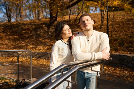 Téléchargez les photos : Joyeux couple avec un stand de chien sur les escaliers du parc, ils admirent le paysage d'automne - en image libre de droit