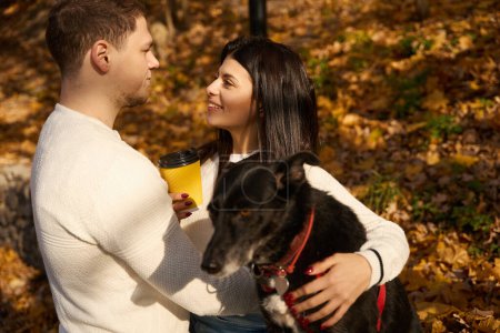 Foto de Mujer feliz charlando con su novio en el parque de otoño, que están paseando a su amado perro - Imagen libre de derechos