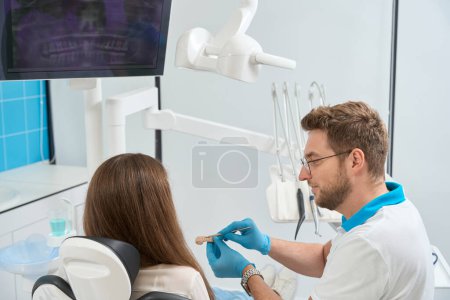Téléchargez les photos : Dentiste pointant avec outil médical au tartre entre les incisives maxillaires sur les dents du modèle au client - en image libre de droit