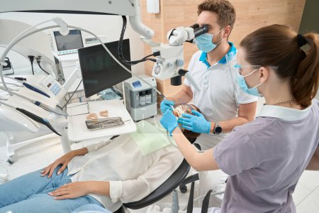 Photo for Experienced dentist removing tartar between central incisors on patient assisted by female nurse - Royalty Free Image