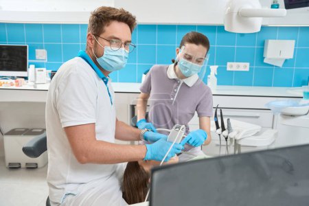 Photo for Dentist looking at computer monitor scanning patient teeth with intraoral scanner assisted by female nurse - Royalty Free Image