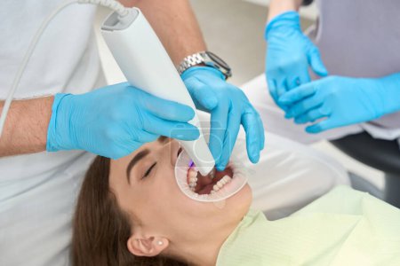 Foto de Dentista dirigiendo escáner intraoral digital en dientes anteriores maxilares de paciente femenina supervisada por asistente - Imagen libre de derechos