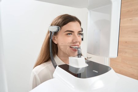 Photo for Calm young female patient undergoing dental cone-beam computed tomography in medical facility - Royalty Free Image