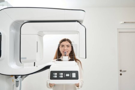 Téléchargez les photos : Femme tranquille subissant une tomodensitométrie à faisceau conique dentaire dans un centre médical - en image libre de droit