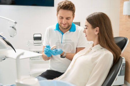 Foto de Odontólogo sonriente demostrando dientes delanteros superiores sanos en el modelo maxilar al cliente - Imagen libre de derechos