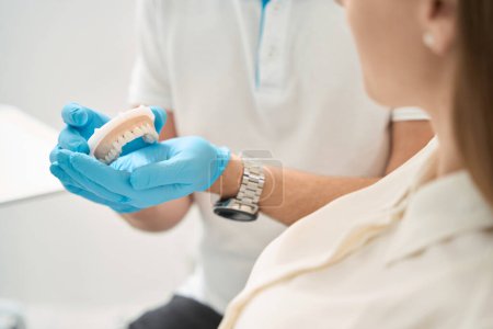 Téléchargez les photos : Photo recadrée du dentiste montrant une dentition antérieure supérieure saine sur le modèle maxillaire au patient - en image libre de droit