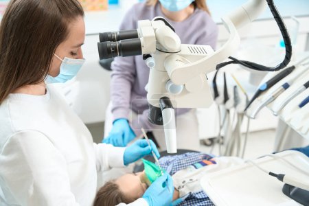 Téléchargez les photos : Nettoyage des canaux dentaires dans la clinique dentaire moderne est effectuée avec anesthésie, au microscope, le dentiste travaille avec assistant - en image libre de droit