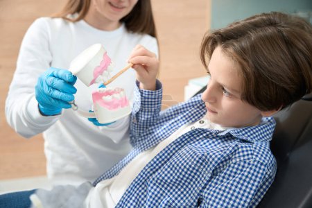 Téléchargez les photos : Garçon apprend à bien prendre soin de ses dents et appareils, le dentiste utilise du matériel visuel - en image libre de droit