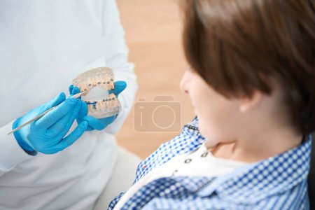 Téléchargez les photos : Hygiéniste dentaire enseigne les méthodes adolescentes de brossage des dents et des appareils orthopédiques, médecin utilise du matériel visuel - en image libre de droit