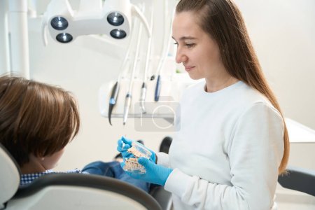 Higienista dentista sonriente enseña a los niños métodos de cepillado de dientes y aparatos ortopédicos, el médico utiliza la dentición simulada