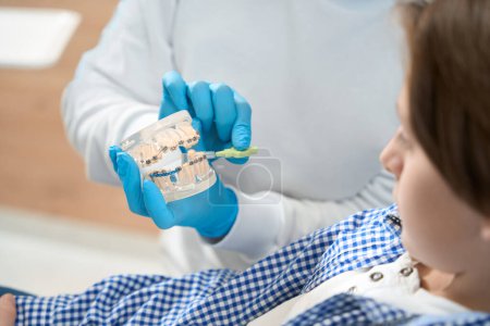 Téléchargez les photos : Le dentiste enseigne aux garçons les méthodes de brossage des dents et des appareils dentaires, le médecin utilise du matériel visuel - en image libre de droit