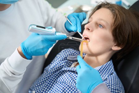 Foto de Niño en una silla de dentista recibe una ambulancia para un dolor de muelas, un especialista utiliza herramientas especiales - Imagen libre de derechos