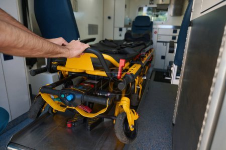 Foto de El hombre agarró la barandilla de la camilla automatizada para el paciente y la saca del transporte médico de trabajo - Imagen libre de derechos